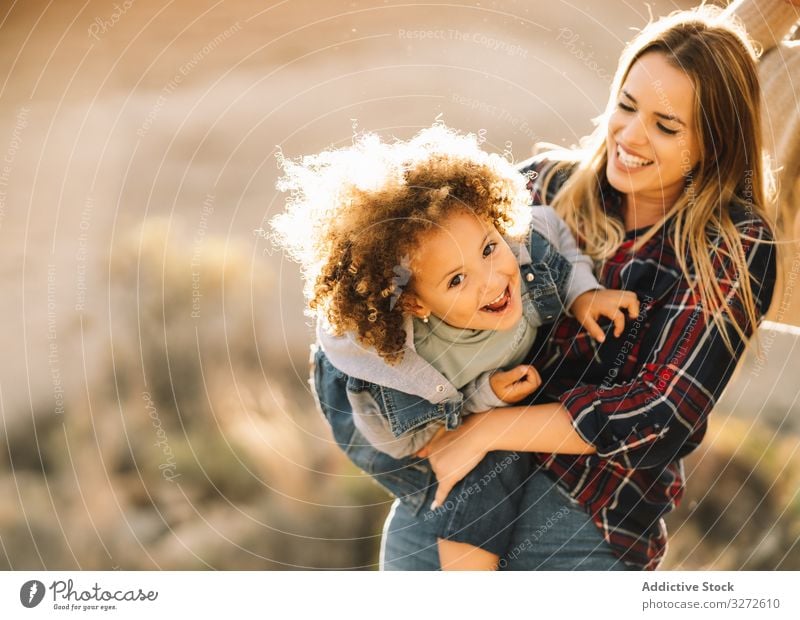 Cheerful woman play with toddler on nature child cuddle hold embrace smile happy tickle cheerful expression curly hair indulge mother fun rest parent lifestyle