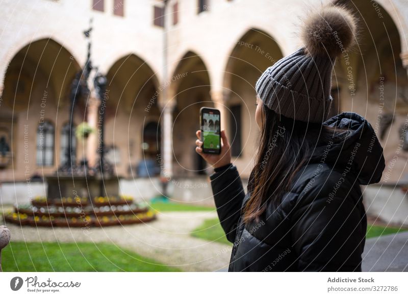 Content Asian female traveler in warm wear taking photo on smartphone while sightseeing at old city woman tourism picture historical architecture using mobile