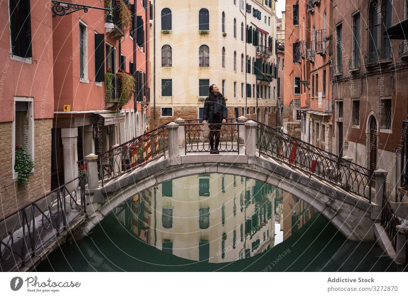 Satisfied resting woman delighting in vacation on small bridge above waterway tourism city canal building old historical standing fun architecture enjoy smile