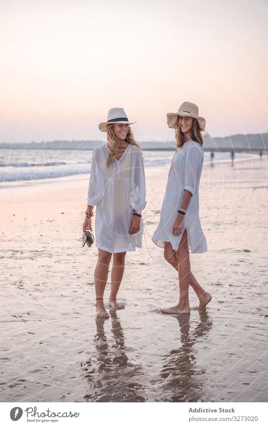 Smiling girlfriends in summer clothes barefoot in water on beach women sea traveling seaside charming vacation hat curly holiday together freedom journey female