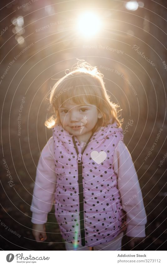 Adorable cute girl in jacket looking at camera in park vest heart cheerful childhood active fun sunlight nature joy activity enjoyment playful kid enthusiastic