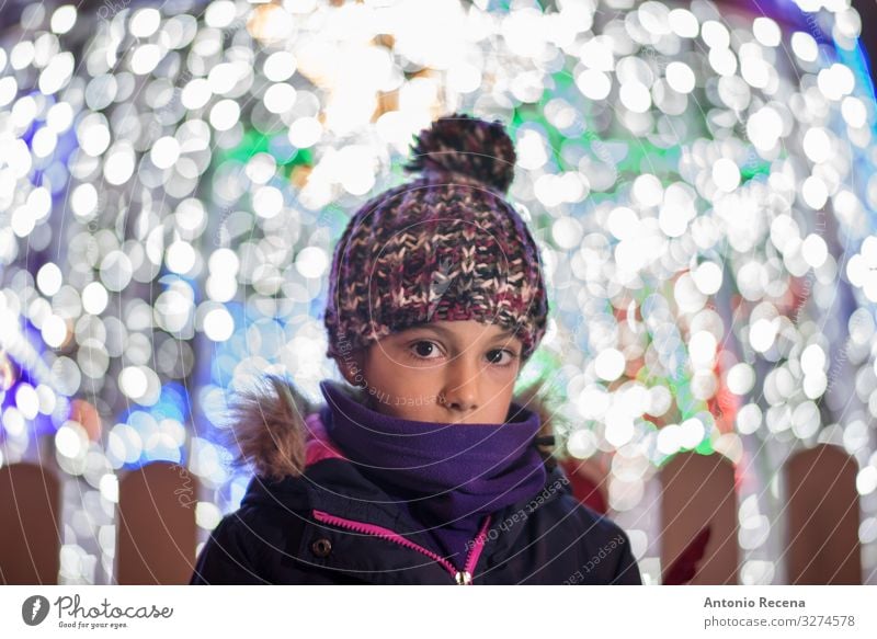 Portrait of shy girl with lights of christmas Lifestyle Joy Winter Decoration Child Infancy Warmth Coat Scarf Hat Cute holidays cold illusion lighting wool hat