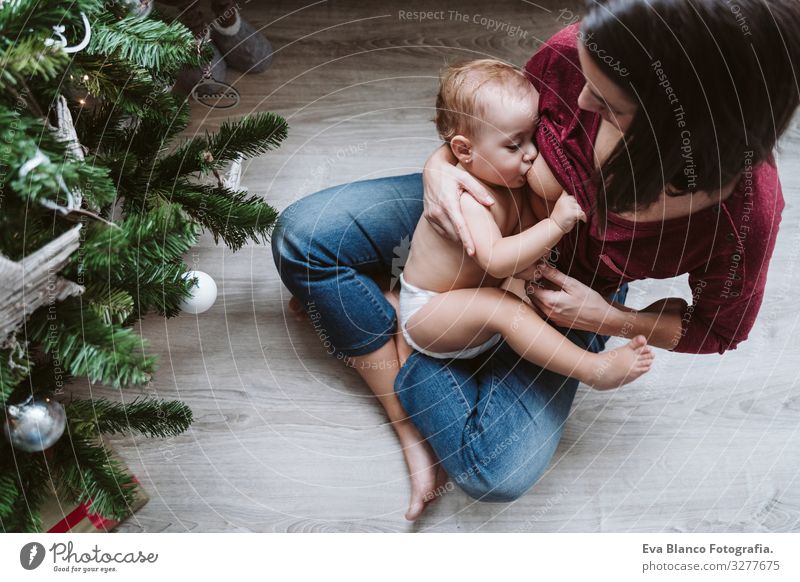 mother breastfeeding her baby girl by the Christmas tree Appease To feed Eating Natural Food Mother motherhood Happy Cute Baby Girl one year decorating