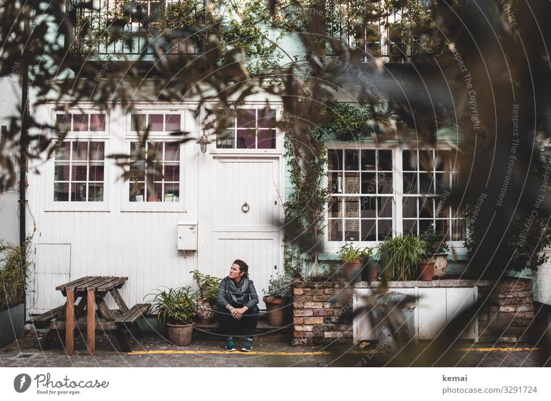 Woman sitting on stairs in front of the house urban Town Facade Window Sit Wait look Door front door Stage Table Bushes relaxed Break Relaxation Adults