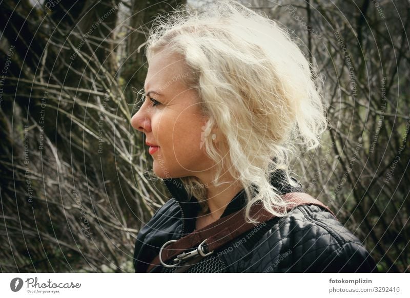 Portrait of a blonde woman with dog leash in front of bare bushes portrait Woman feminine Self-confident Face of a woman look expect expecting Blond Dog lead