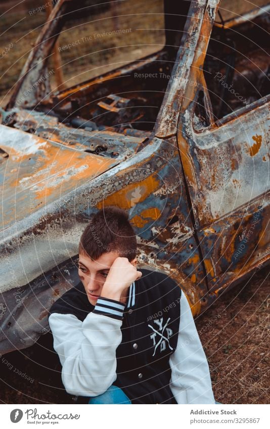 Young woman resting near rusty car rebel relax countryside burnt young lifestyle freedom sit ground vehicle auto androgynous touch short hair subculture