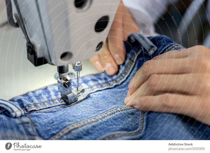 Woman's hands in textile factory sewing on industrial sewing machine. industry clothing manufacturing worker woman fabric pants blue jeans occupation production