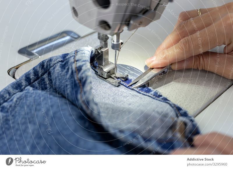 Woman's hands in textile factory sewing on industrial sewing machine. industry clothing manufacturing worker woman fabric pants blue jeans occupation production