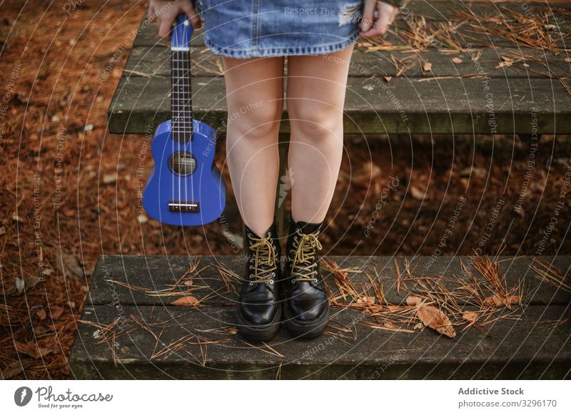 Young woman with ukulele on wooden stairs in park teenager guitar autumn boot music alone instrument small equipment shoes hand pine needles guitarist black