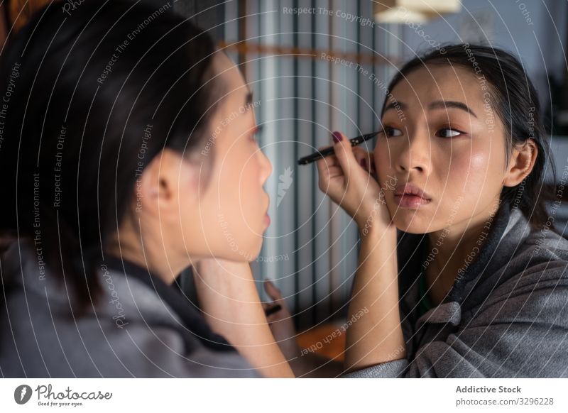 Asian woman applying eyeliner in front of mirror makeup cosmetic casual beauty eyes reflection young female face fashion care complexion facial cosmetology