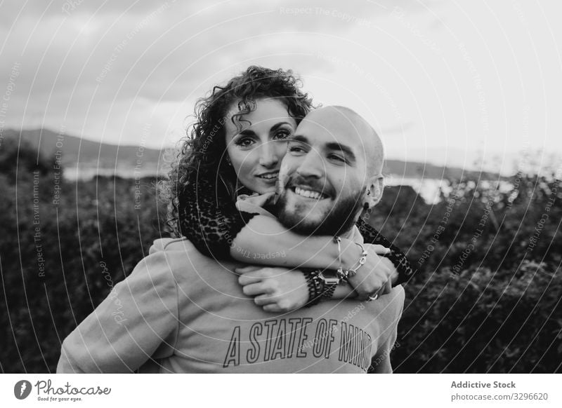 Young couple in love walking on rural road and having fun piggyback seaside field nature green grass playful cheerful joyful laugh carrying embrace ride path