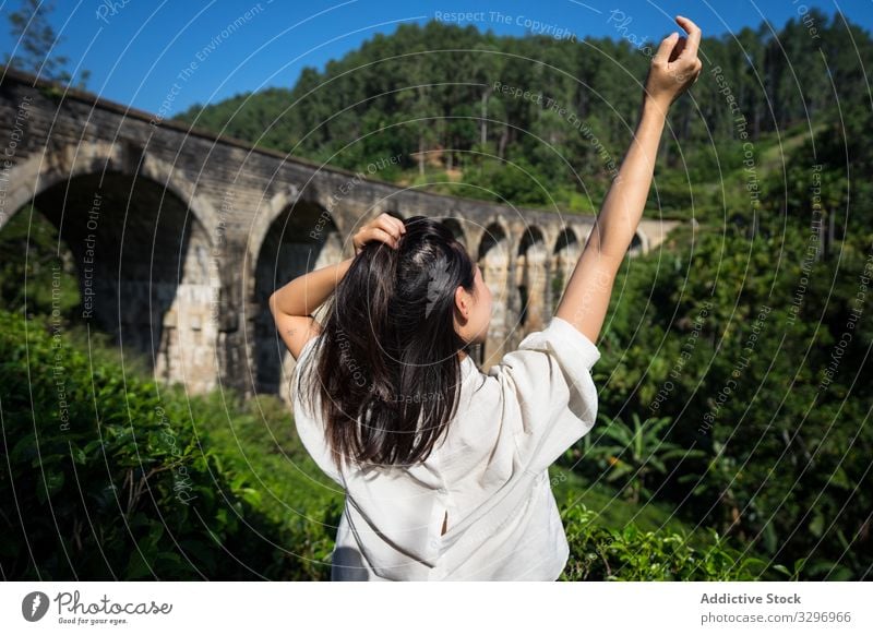 Young woman touching hair and enjoying landscape of ancient bridge green forest old asian nine arches bridge shabby ella sri lanka touristic travel