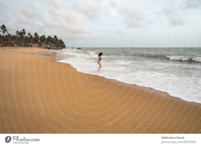 Anonymous peaceful woman at lonely seaside tourism seashore ocean travel beach walking empty sand female explore view sky cloud wave negombo sri lanka coastline