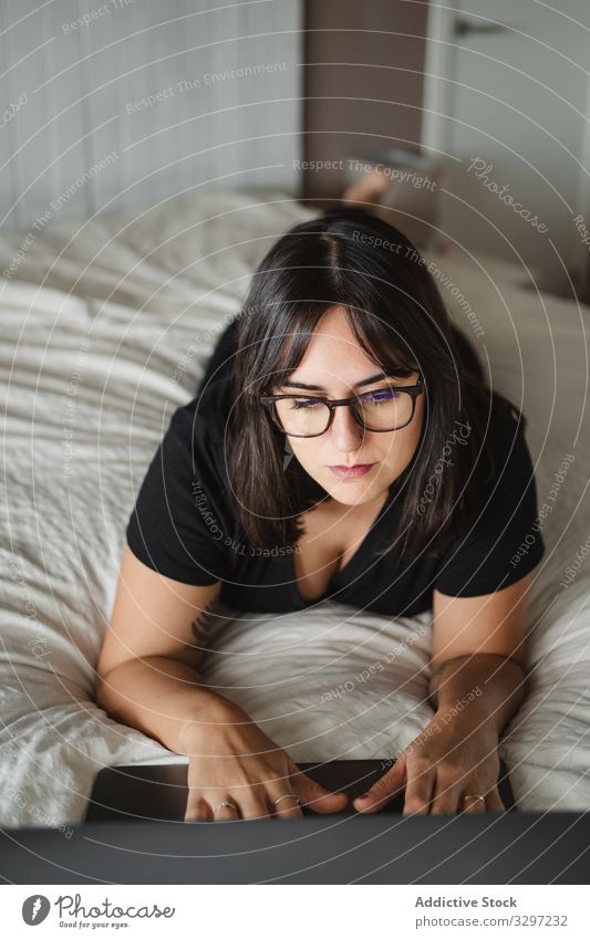 Focused young female student using laptop on bed at home woman typing study lying education communication connection contact internet online surfing browsing