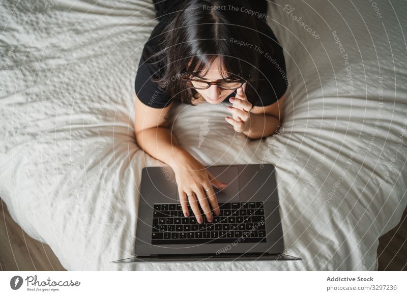 Focused young female student using laptop on bed at home woman typing study lying education communication connection contact internet online surfing browsing