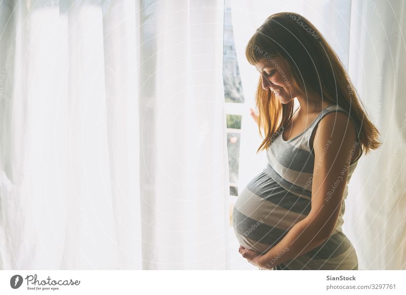 Young beautiful pregnant woman standing near window at home Lifestyle Happy Beautiful Body Hair and hairstyles Skin Face Healthy Health care Living or residing