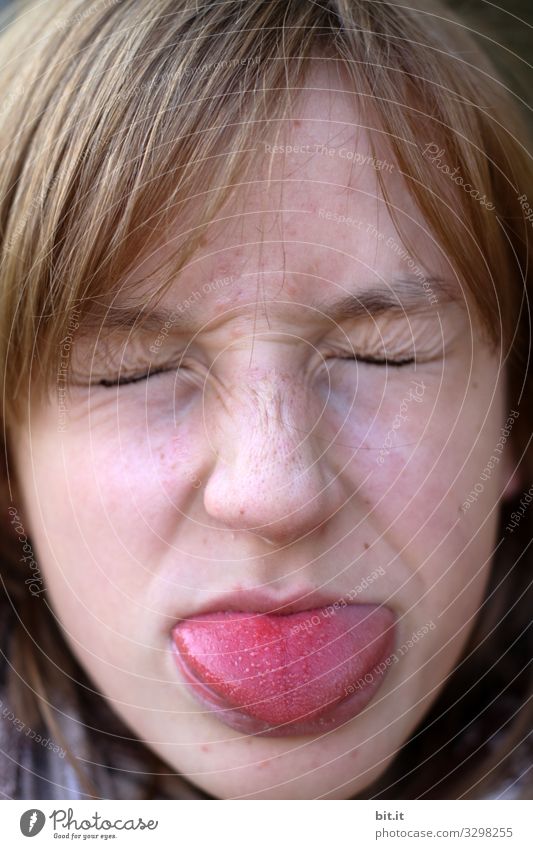 Girl, young woman with closed eyes, sticks out red tongue. Tongue is red colored by food, paint, candy, berries or other food. Eyes are closed, facial expressions are distorted from the face, to a funny expression.