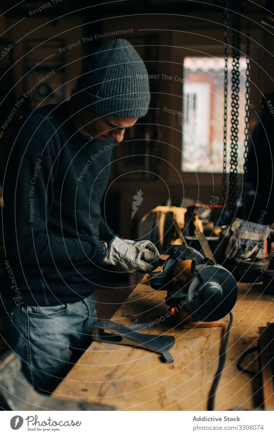 Crop craftsman checking axe in workshop blade grinder sharpen using tool male metalwork industry handmade machine electric guy electrical busy job heavy worker