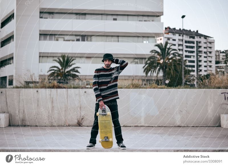 Young stylish man with skateboard standing in city street building hipster young modern contemporary active male urban millennial sport recreation guy longboard