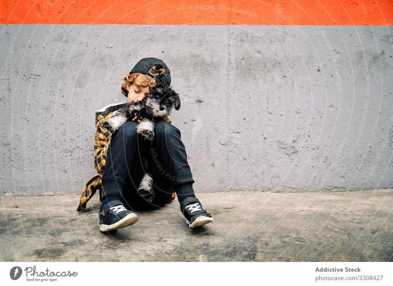 Boy with puppy sitting next to concrete wall child dog boy street building affection care little breed canine purebred animal cuddle domestic friendly kid pet