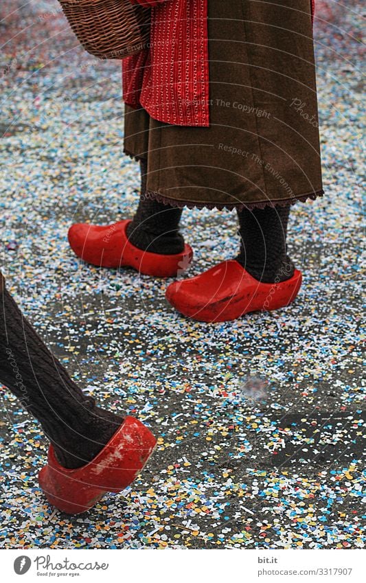 Three legs stand and walk in red Dutch clogs; clogs and apron dressed up in the street covered with confetti, on Mardi Gras during a carnival parade, the traditional Buernfasnachtin Südbaden.