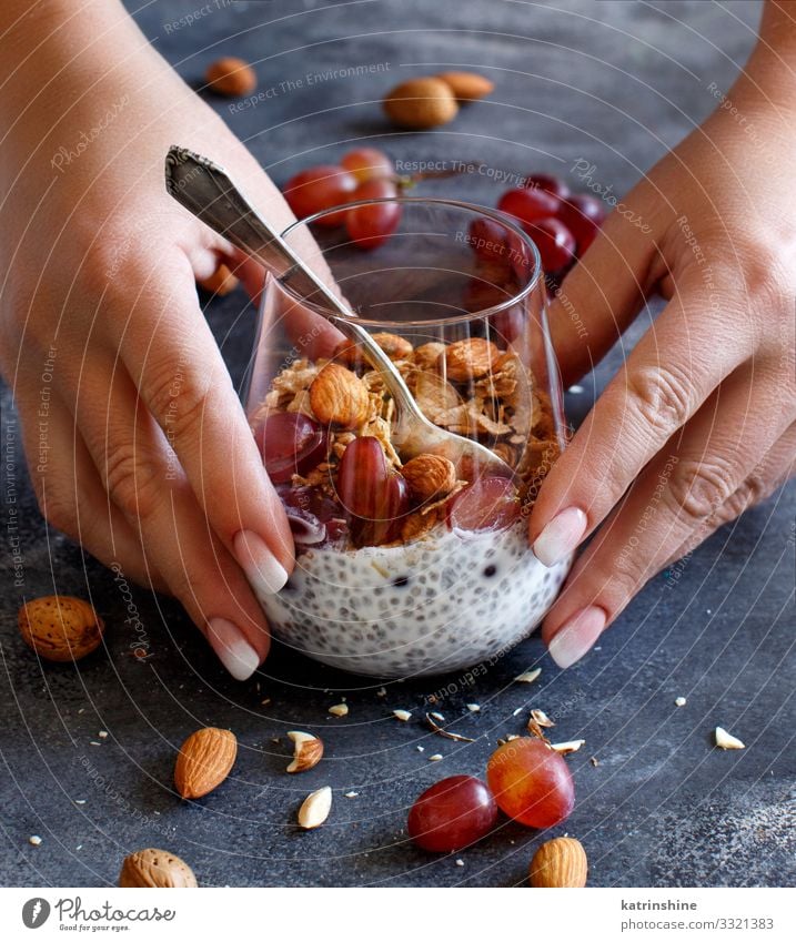 Chia pudding parfait with red grapes and almonds Yoghurt Fruit Dessert Eating Breakfast Diet Spoon Hand Dark Gray White jar chia Bunch of grapes nuts Faceless