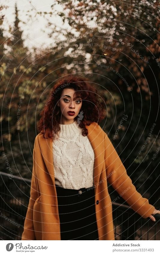 Pensive curly haired woman wearing casual standing in park pensive sensual young dark hair overcoat jumper railing knitted female thoughtful thinking trendy