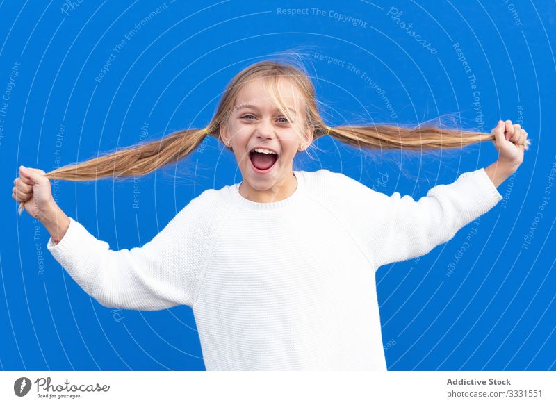 Overjoyed girl holding pigtails and laughing fun pull crazy hair blond kid smile enjoy casual child carefree happy beautiful female lifestyle opened mouth