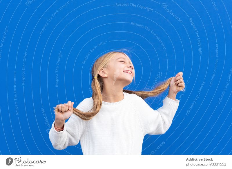 Overjoyed girl holding pigtails and laughing fun pull crazy hair blond kid smile enjoy casual child carefree happy beautiful female lifestyle opened mouth