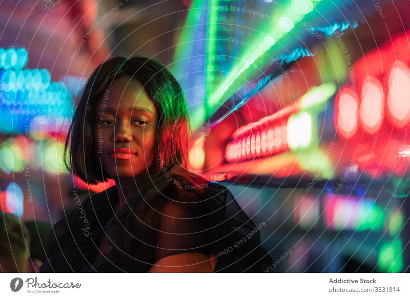 Cheerful black woman on funfair smile night arcade illumination sit rest weekend ethnic female amusement attraction colorful joy happy cheerful bright lady