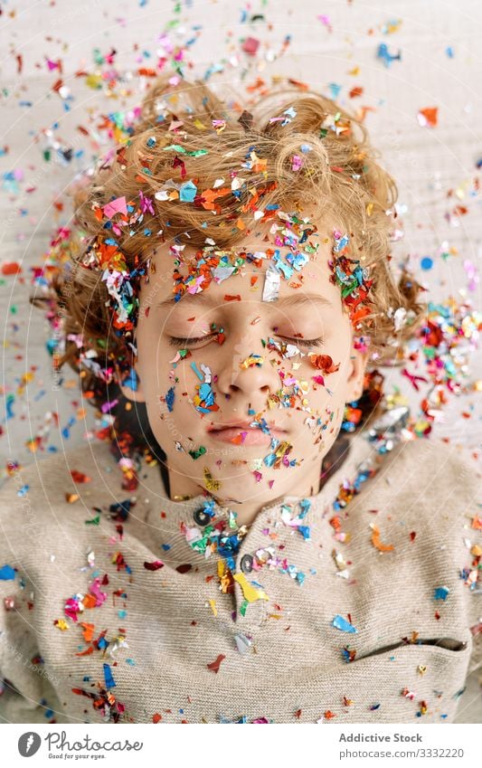 Beautiful boy with face covered in confetti home emotionless fun colorful lying preteen floor modern childhood lifestyle celebrate holiday festive event