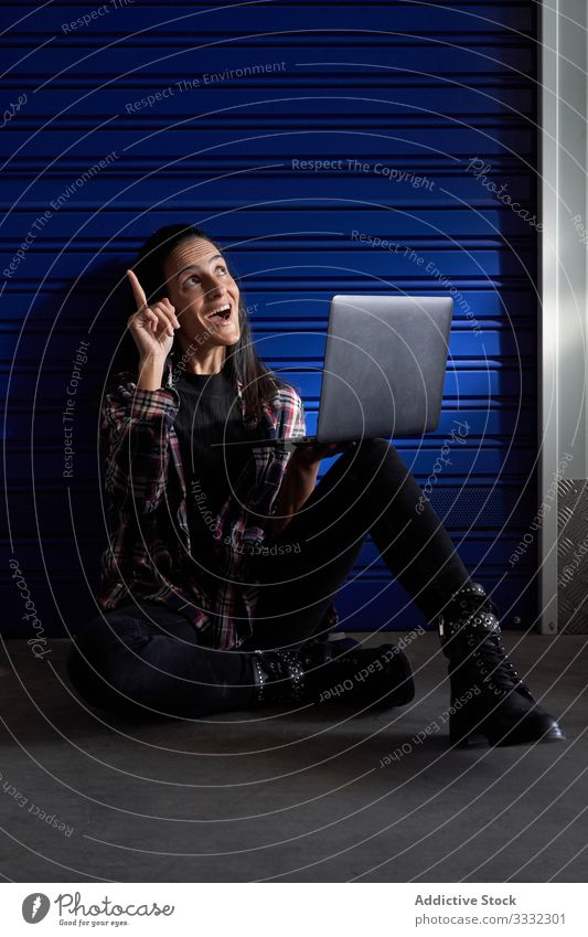 Beautiful brunette woman with plaid shirt and black pants sitting in front of the door of a storage room. He has a portal computer with which he works and organizes the moving boxes