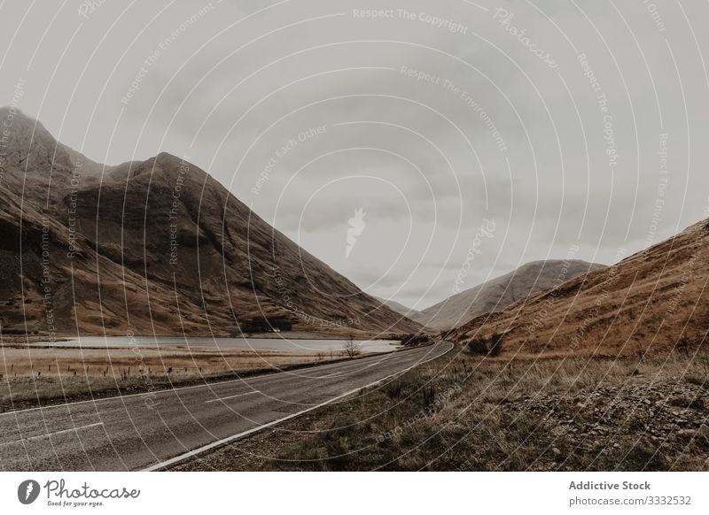 Empty road riding along river surrounded by mountain valley hill travel nature landscape sky tourism adventure gray dangerous extreme journey scenery vacation