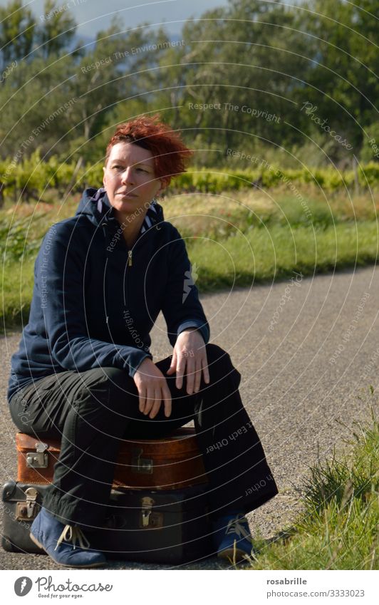 ordered and not picked up | taken literally | - middle-aged woman sitting waiting on packed suitcases on a narrow country road in the countryside with wind