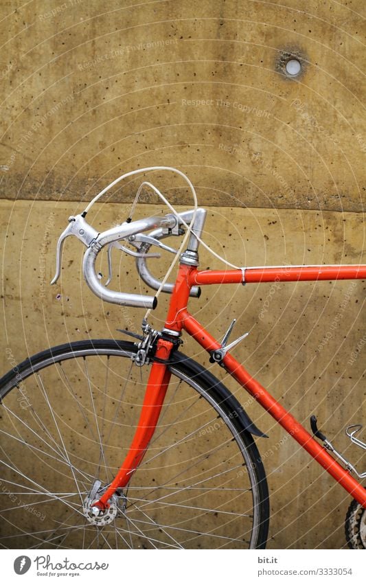 Orange racing bike from a sporty hipster, standing during a break, parked in front of a brown wall, in the neckline you can see handlebars, tires, front wheel, brake and frame of the bike in the old, retro style.