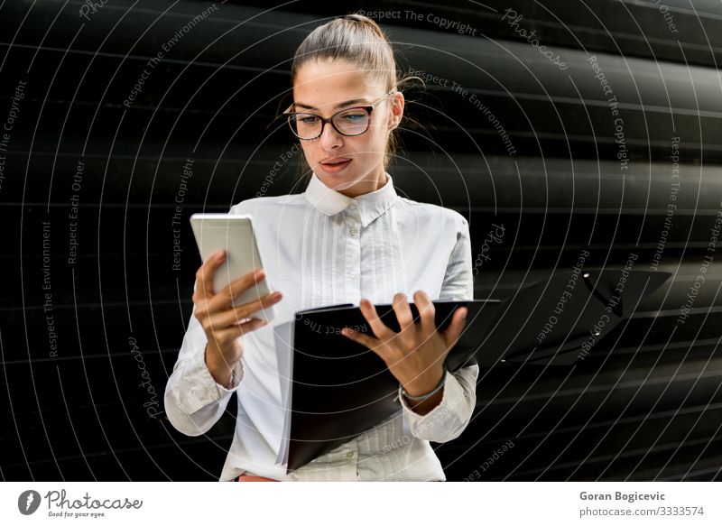 Pretty young businesswoman using mobile phone and holding file Lifestyle Beautiful Work and employment Office Business Telephone PDA Technology Human being