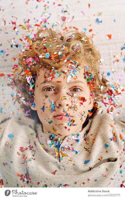 Beautiful boy with face covered in confetti home emotionless fun colorful lying preteen floor modern childhood lifestyle celebrate holiday festive event