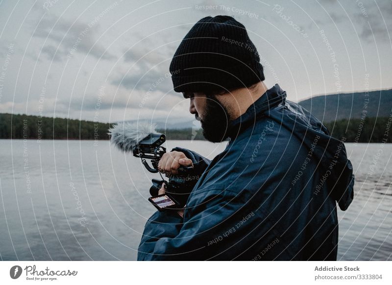 Focused man reviewing photos on camera using videographer river forest nature focused busy serious beach male journey hill water travel day freedom cloudy