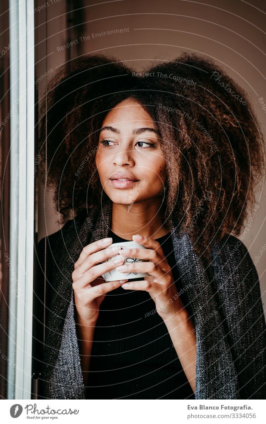 portrait of beautiful afro american young woman by the window holding a cup of coffee. Lifestyle indoors African-American Woman Coffee Home Ethnic