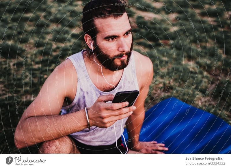 young man in a park listening to music on mobile phone and headset after practicing yoga sport. city background. healthy lifestyle. Music Cellphone Technology