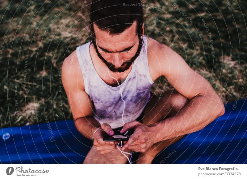 young man in a park listening to music on mobile phone and headset after practicing yoga sport. city background. healthy lifestyle. Music Cellphone Technology