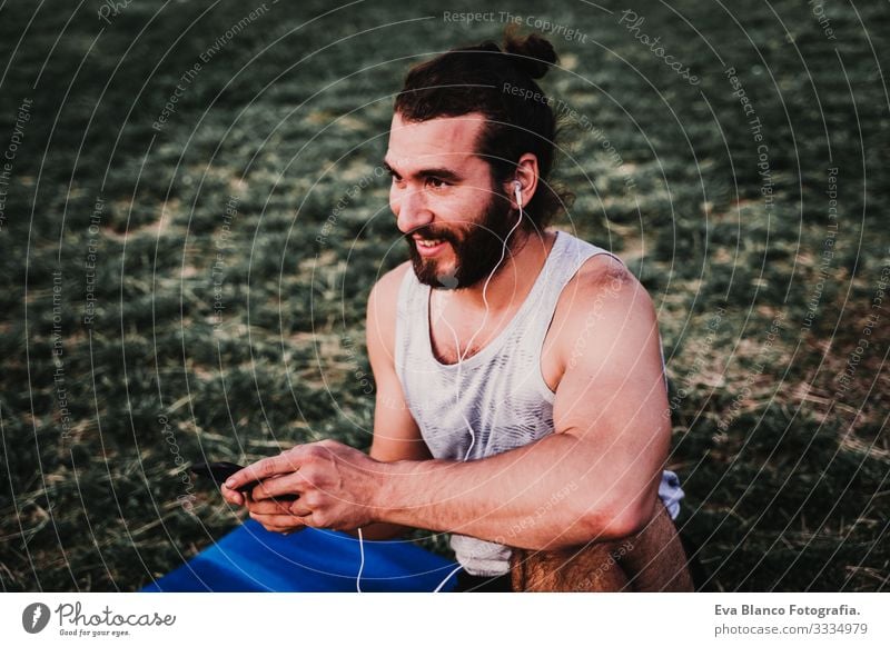 young man in a park listening to music on mobile phone and headset after practicing yoga sport. city background. healthy lifestyle. Music Cellphone Technology