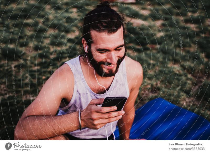 young man in a park listening to music on mobile phone and headset after practicing yoga sport. city background. healthy lifestyle. Music Cellphone Technology