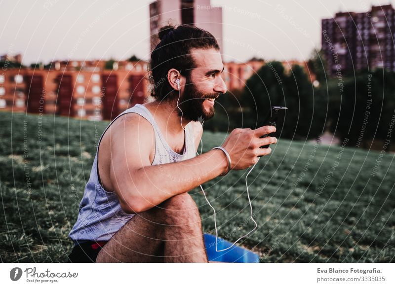 young man in a park listening to music on mobile phone and headset after practicing yoga sport. city background. healthy lifestyle. Music Cellphone Technology