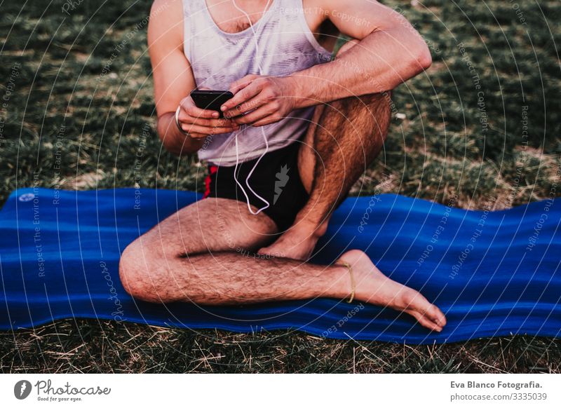 young man in a park listening to music on mobile phone and headset after practicing yoga sport. city background. healthy lifestyle. Music Cellphone Technology