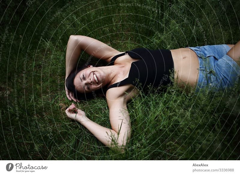 Young woman lies in the grass and laughs Joy Beautiful Life Trip Youth (Young adults) 18 - 30 years Adults Plant Summer Beautiful weather Grass Top Brunette