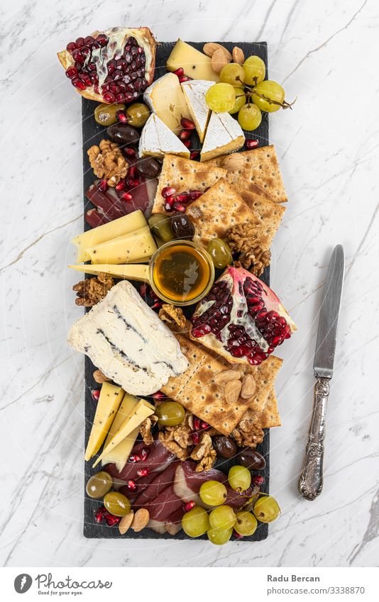 Food Platter With Truffle Cheese, Duck Breast, Brie Cheese, Pecan Nuts, Pomegranate Seeds, Grapes, Almonds, Honey, Olives and Crackers on White Marble Background