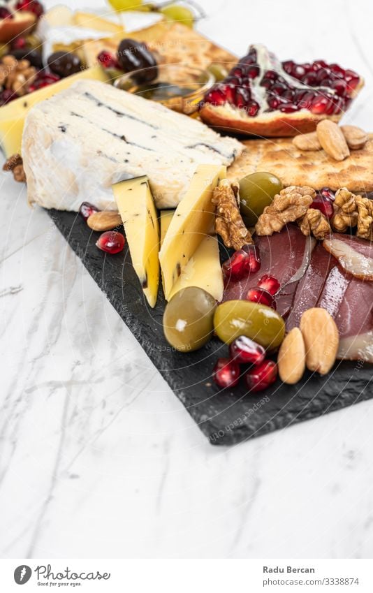 Food Platter With Truffle Cheese, Duck Breast, Brie Cheese, Pecan Nuts, Pomegranate Seeds, Grapes, Almonds, Honey, Olives and Crackers on White Marble Background