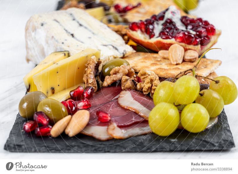 Food Platter With Truffle Cheese, Duck Breast, Brie Cheese, Pecan Nuts, Pomegranate Seeds, Grapes, Almonds, Honey, Olives and Crackers on White Marble Background