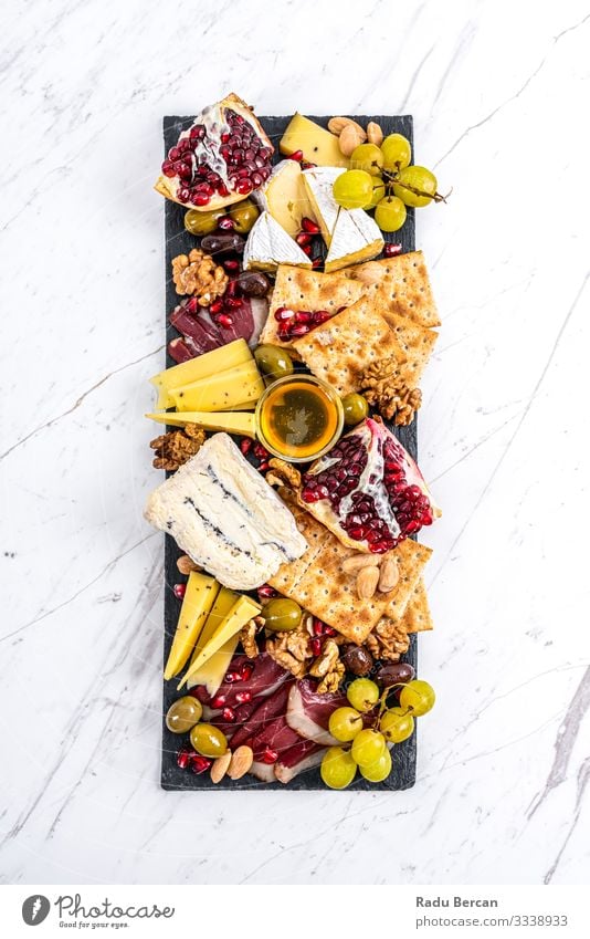 Food Platter With Truffle Cheese, Duck Breast, Brie Cheese, Pecan Nuts, Pomegranate Seeds, Grapes, Almonds, Honey, Olives and Crackers on White Marble Background